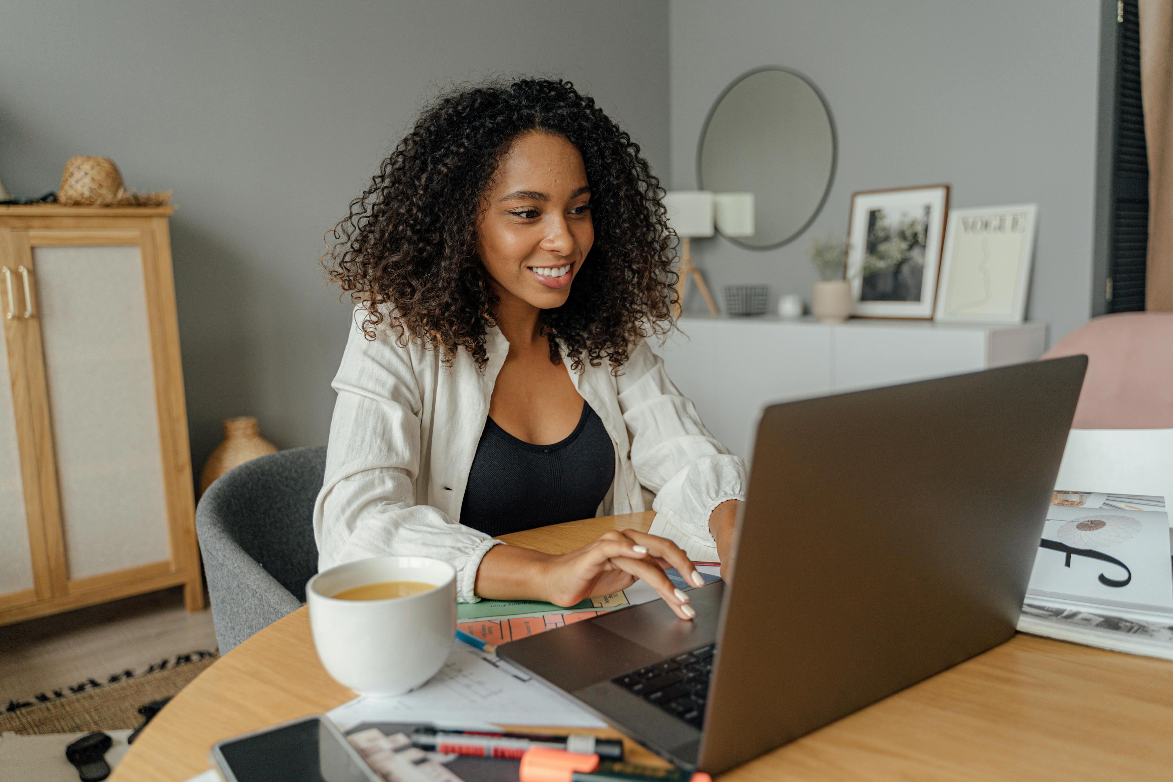Photo - A young lady in front of her laptop computer working with her coffee at her right side.